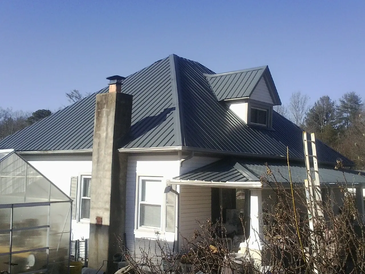 Dark blue standing seam metal roof on a white farmhouse with dormer — Slate & Tile Roof Repair by Roofing Brothers in Mundelein