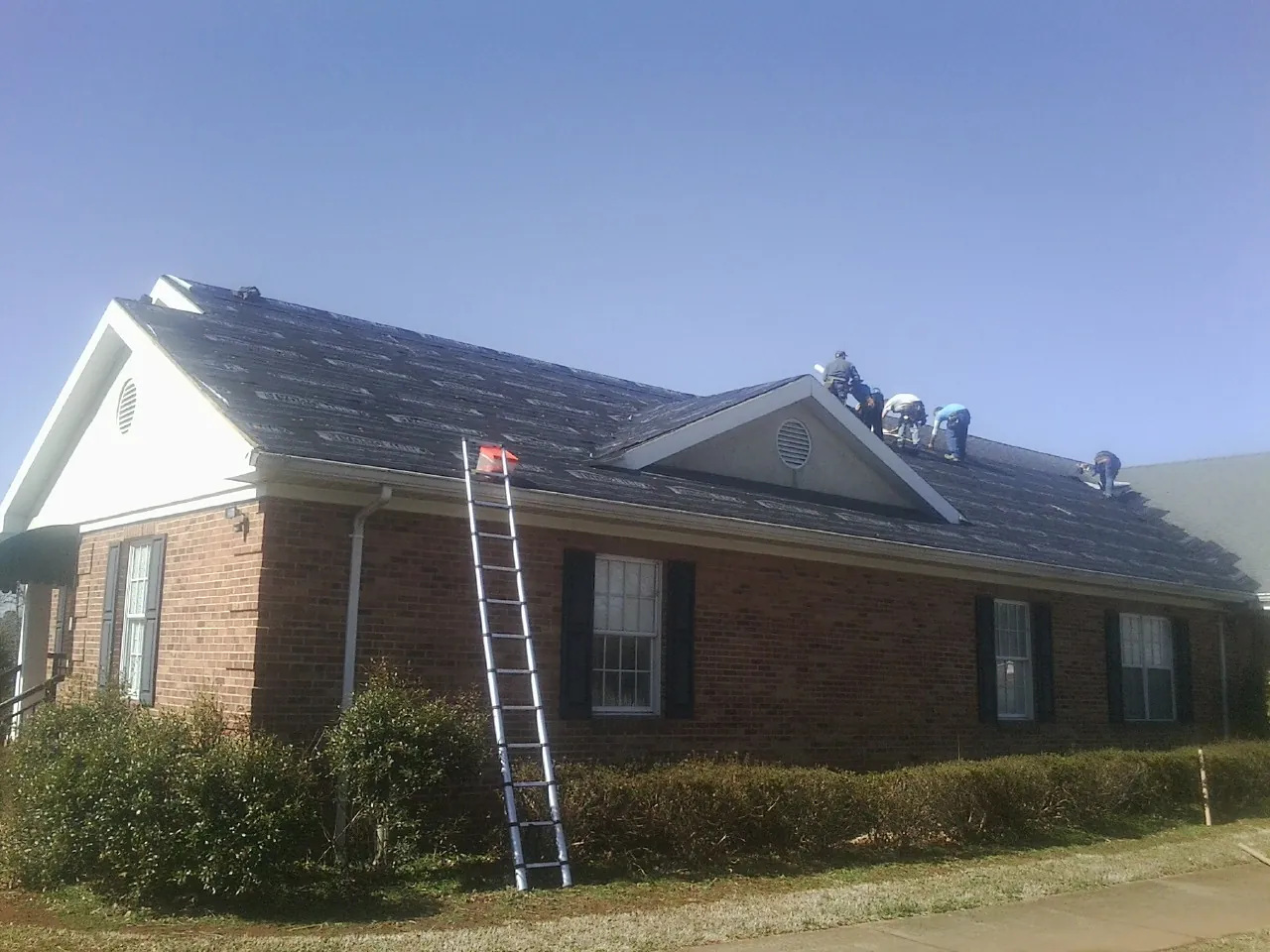 Crew tearing shingles off a brick ranch roof with a ladder set — Emergency Roof Repair work by our crew in Mundelein