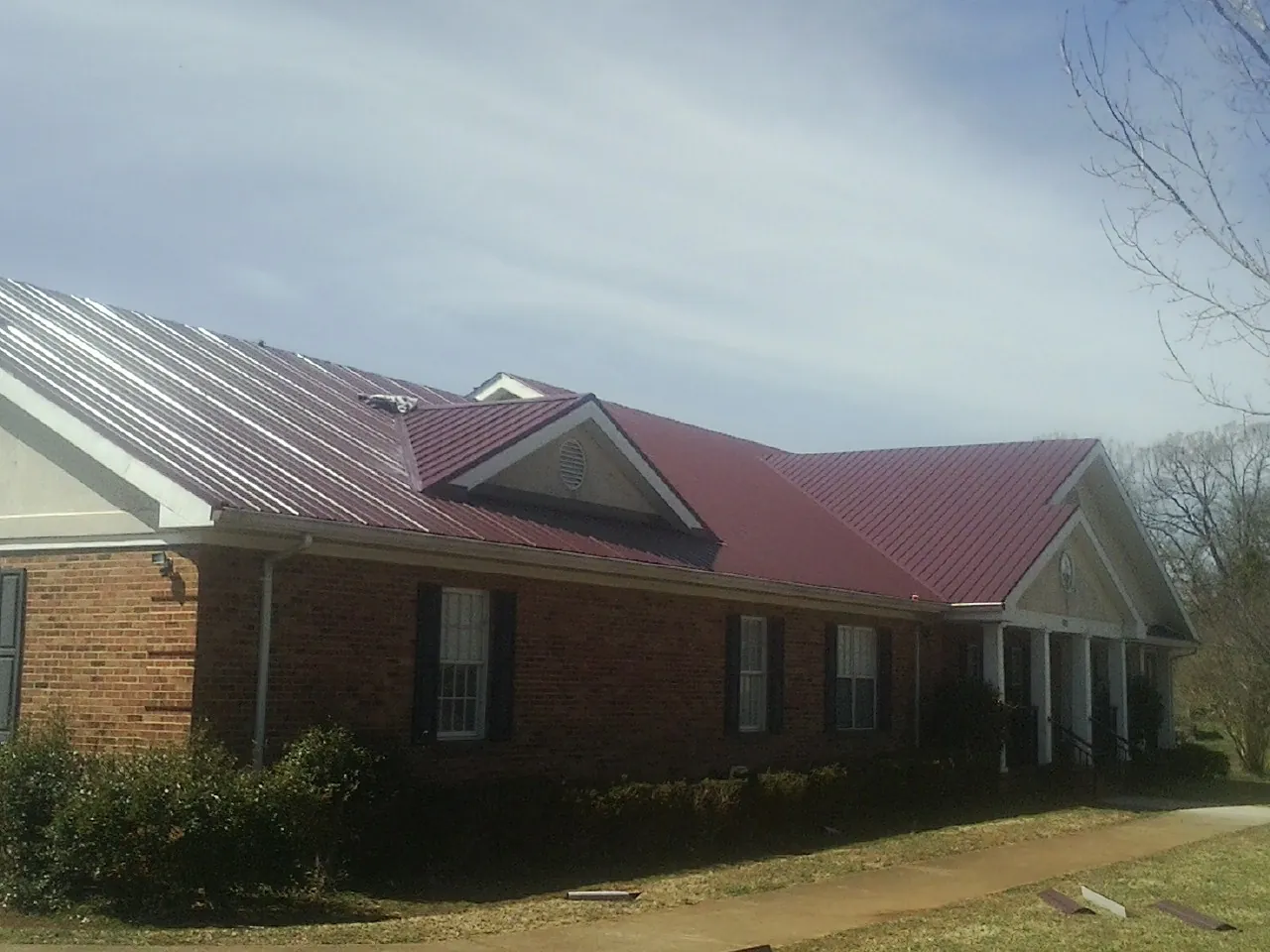 Red metal roof with gabled entries on a long brick building, from a Hail Damage Roof Repair job in Mundelein