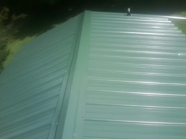 New green metal panels meeting at the ridge of a roof — Flat Roof Repair work by our crew in Mundelein