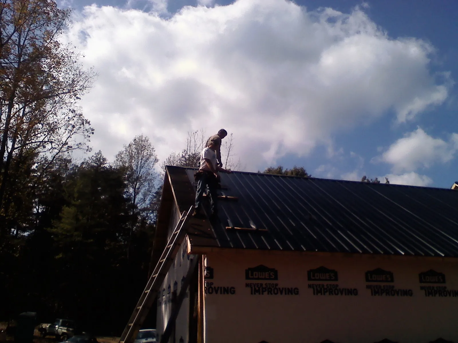 Roofer fastening dark metal panels high against a cloudy sky, from a Roof Inspection job in Mundelein
