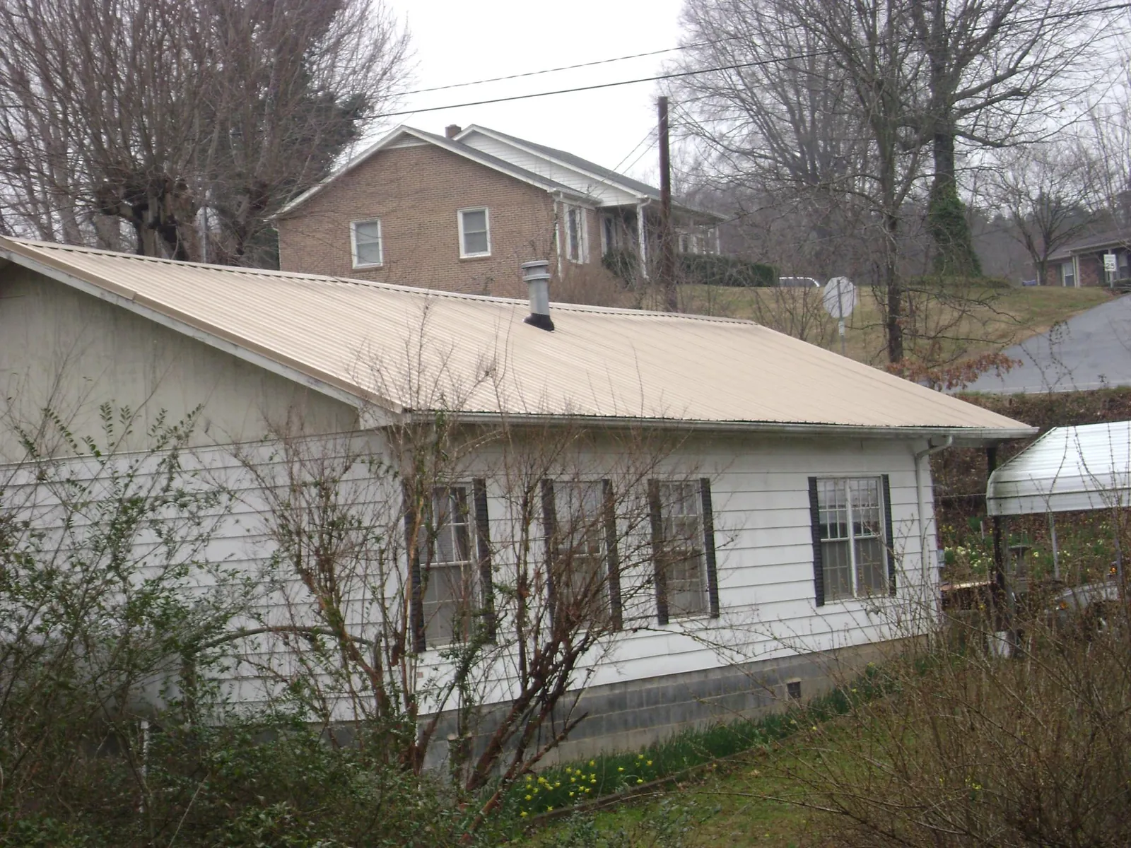 Tan metal roof on a white sided house set into a hillside — Commercial Roofing by Roofing Brothers in Mundelein